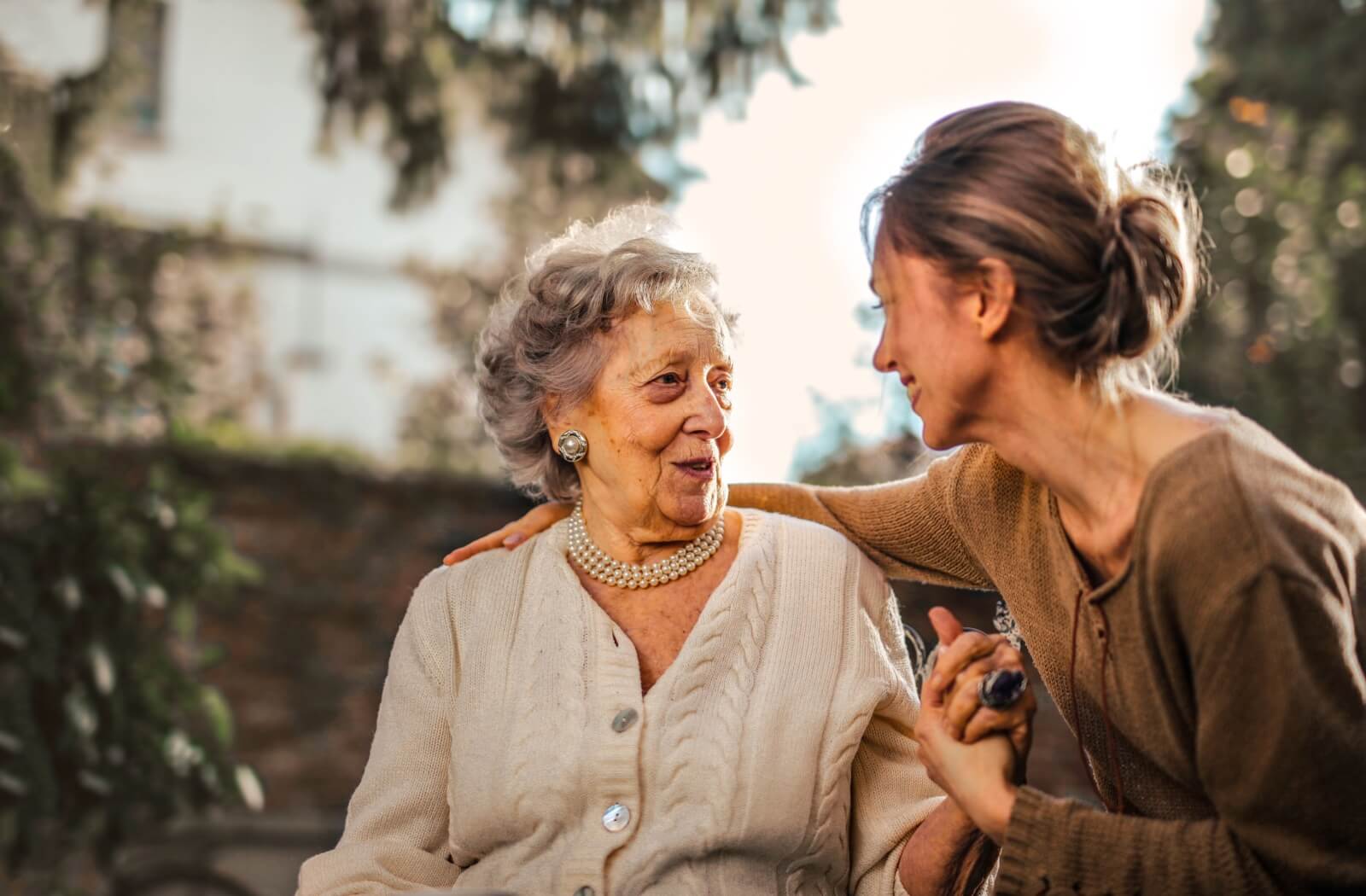 An older woman holding hands with a younger adult woman and looking at each other having a conversation.