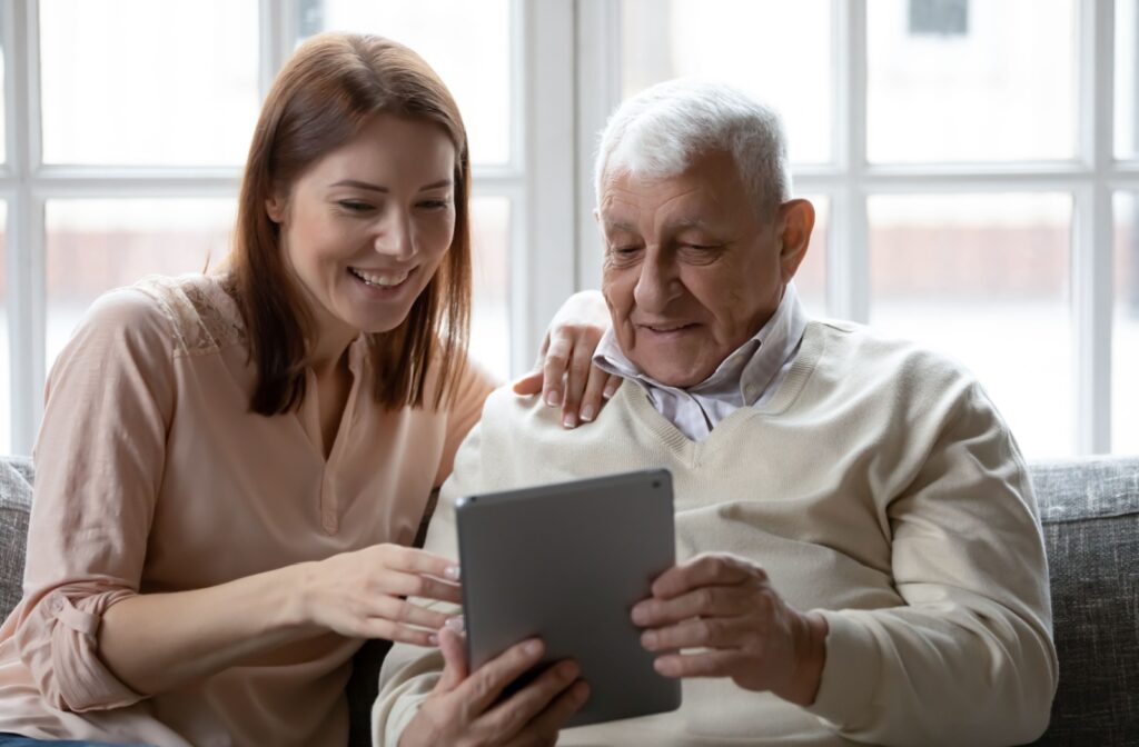 A smiling senior man sitting on the couch with his adult daughter in memory care.