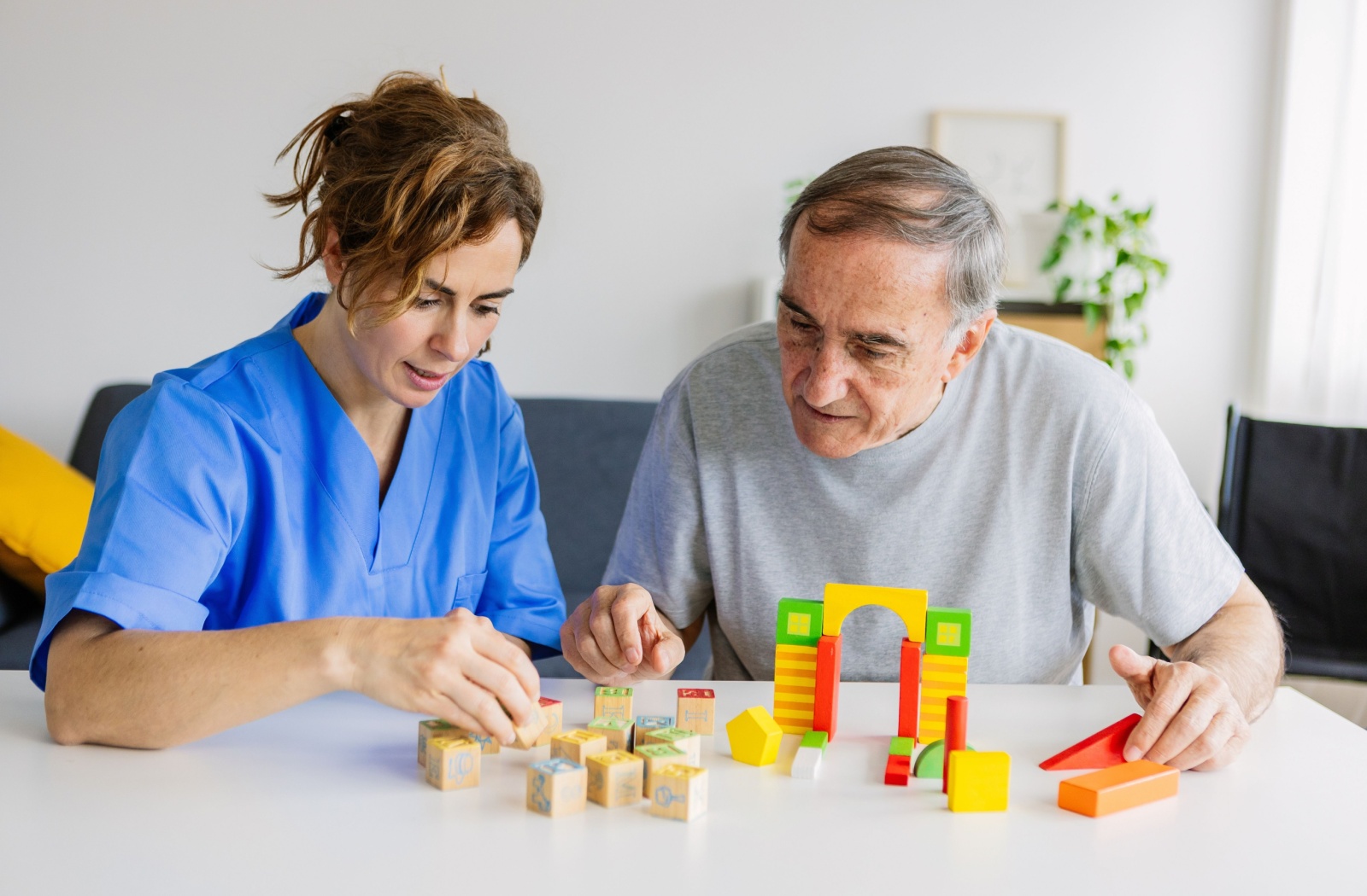 Caregiver working with an elderly man with Alzheimer's, engaging in a cognitive building activity to stimulate memory and maintain motor skills.