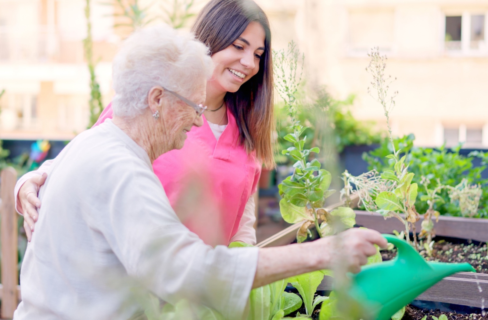 Caretaker assisting senior in a memory care facility while watering a garden.