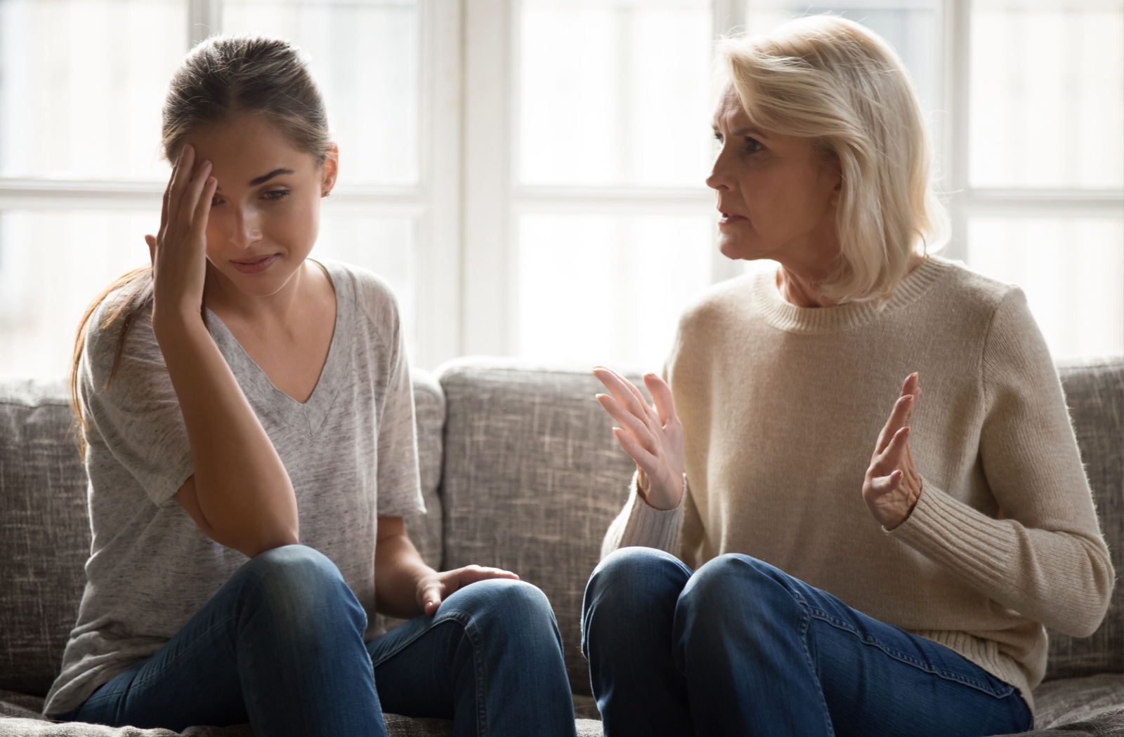 A frustrated adult sits on a couch with their older parent, both increasingly agitated by miscommunication about dementia