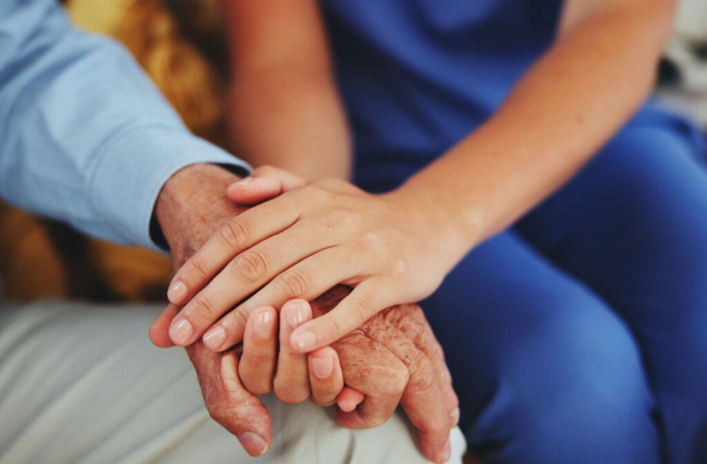 A close-up image of a caregiver clasping a resident's hand in respite care.