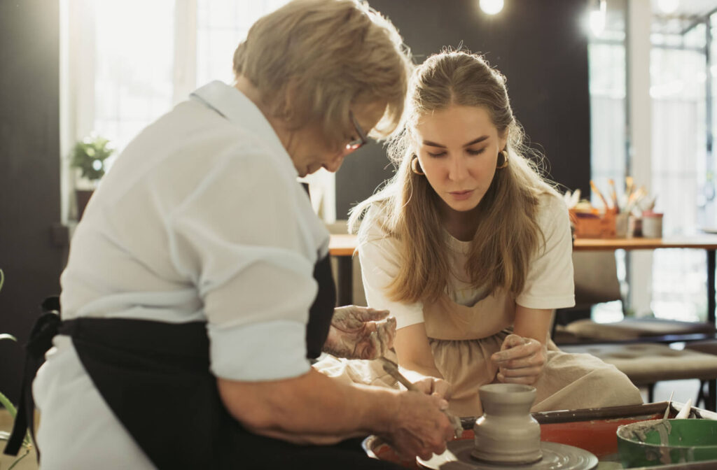 A close-up image of an older adult's hands as they paint small flowers on a blue bowl.