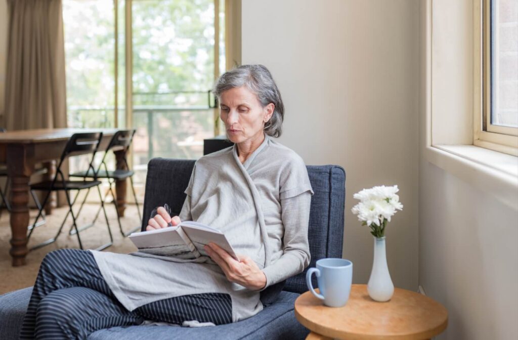 Senior journaling by a bright window with coffee and flowers nearby in a memory care setting