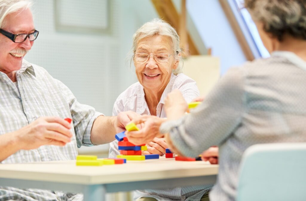 3 older adults laugh together during a board game night in senior living while they work together to build a colored brick structure