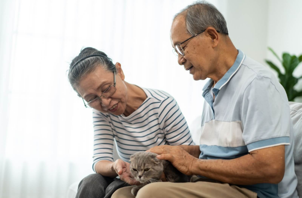 Two seniors in memory care gently pet a small cat as part of a provided pet therapy to provide positive sensory experiences